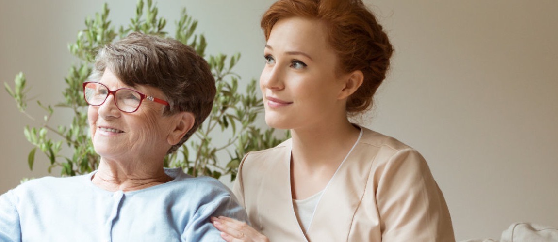 A caregiver sitting beside a senior woman looking out of a window
