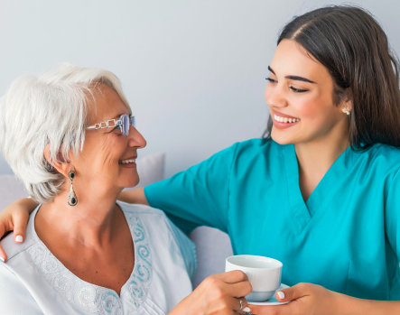 A caregiver in scrubs sharing tea with a senior woman